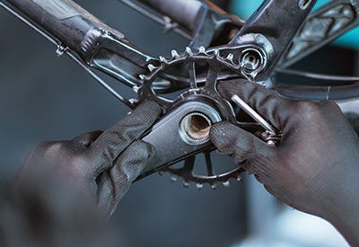 A close up of a front chainring on a mountain bike with a mechanic's hands on it