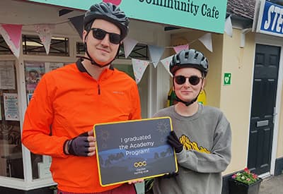 A male and female cycling holding a plaque together