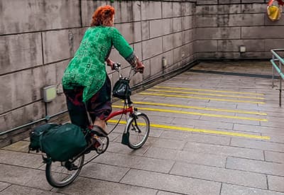 A woman riding a red holding bicycle down a ramp to a subway